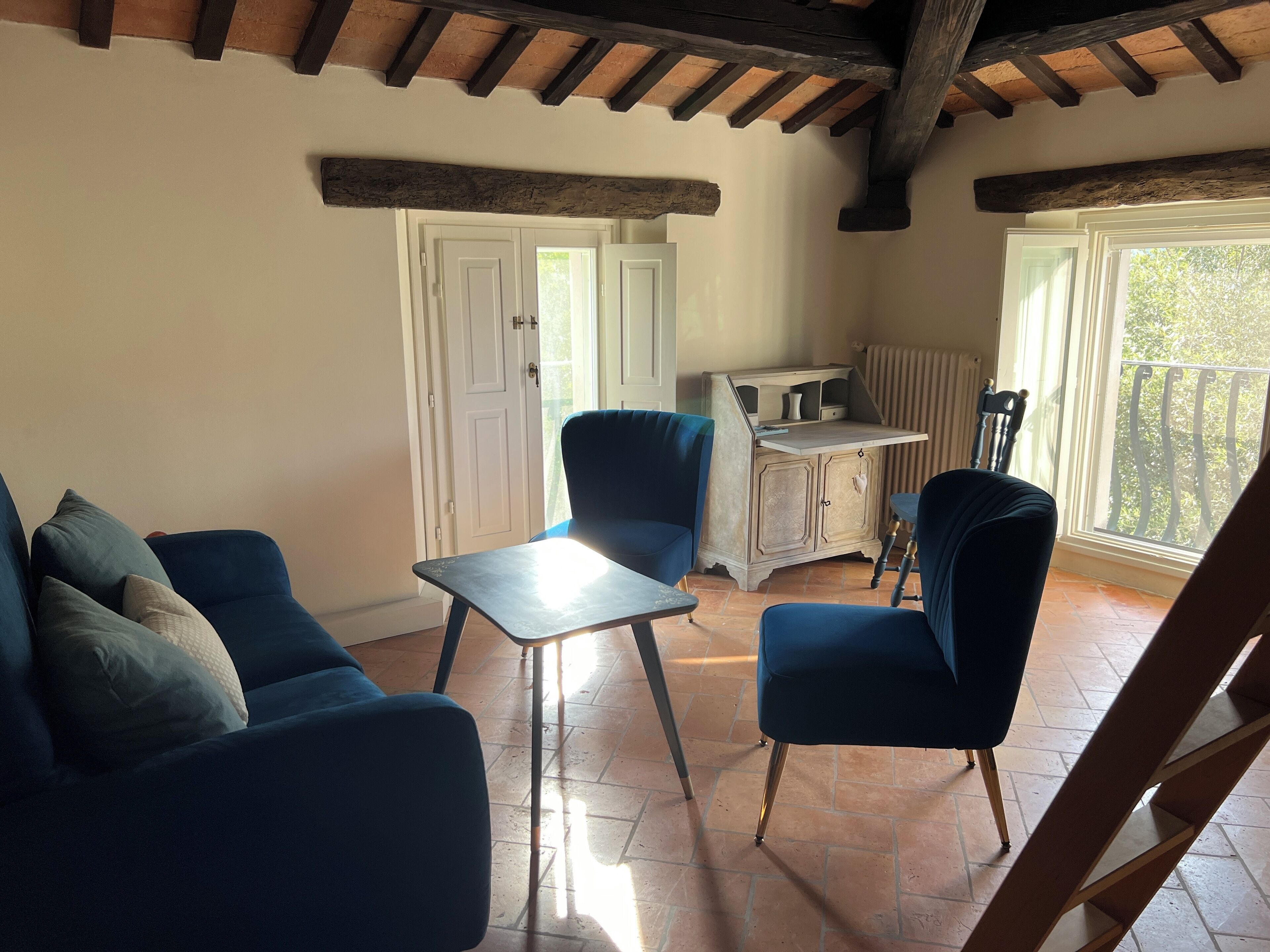 A cozy room with a blue sofa, a small table, and a chair. There's a white door and a window with a view of trees.