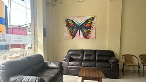 A living room with two black leather sofas, a wooden coffee table, and a colorful butterfly painting on the wall. - DORAL INN HOTEL (Iquitos)