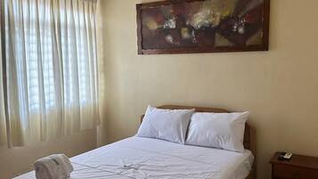 Een hotelkamer met een bed, nachtkastje, airconditioning en een raam met gordijnen.