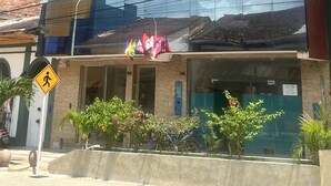 A modern building with a reflective glass facade, a ground-level entrance with flags, and a yellow pedestrian crossing sign. - DORAL INN HOTEL (Iquitos)
