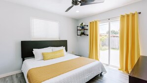 A bedroom with a bed, a ceiling fan, a window with blinds, and a sliding glass door with yellow curtains.