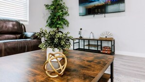 A living room with a wooden coffee table, a potted plant, a leather couch, a TV mounted on the wall, and a decorative item on a side table.