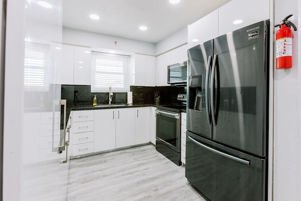 A modern kitchen with white cabinets, stainless steel appliances, and a black countertop.