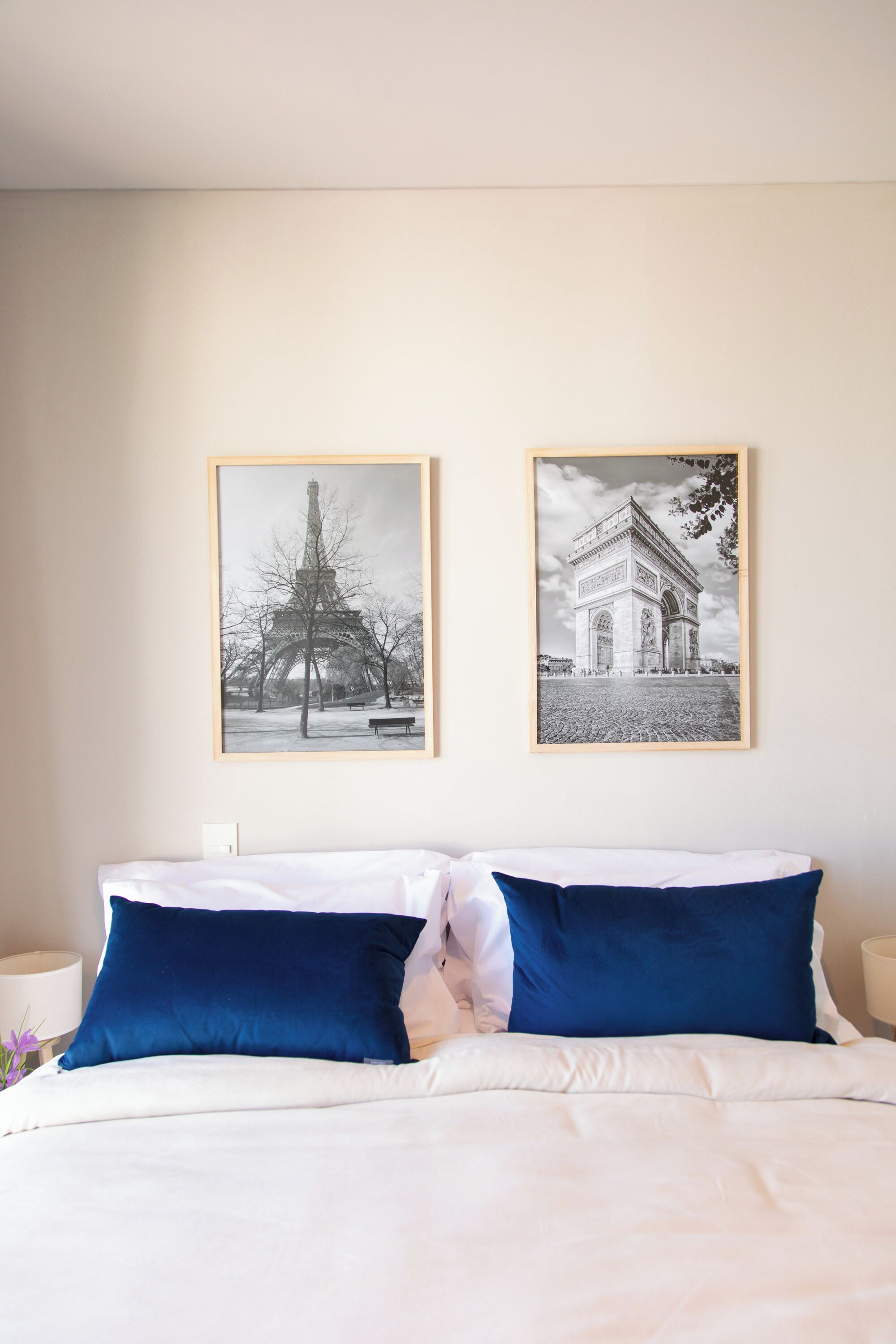 A hotel room with a bed, two pillows, a nightstand, and two framed pictures on the wall.