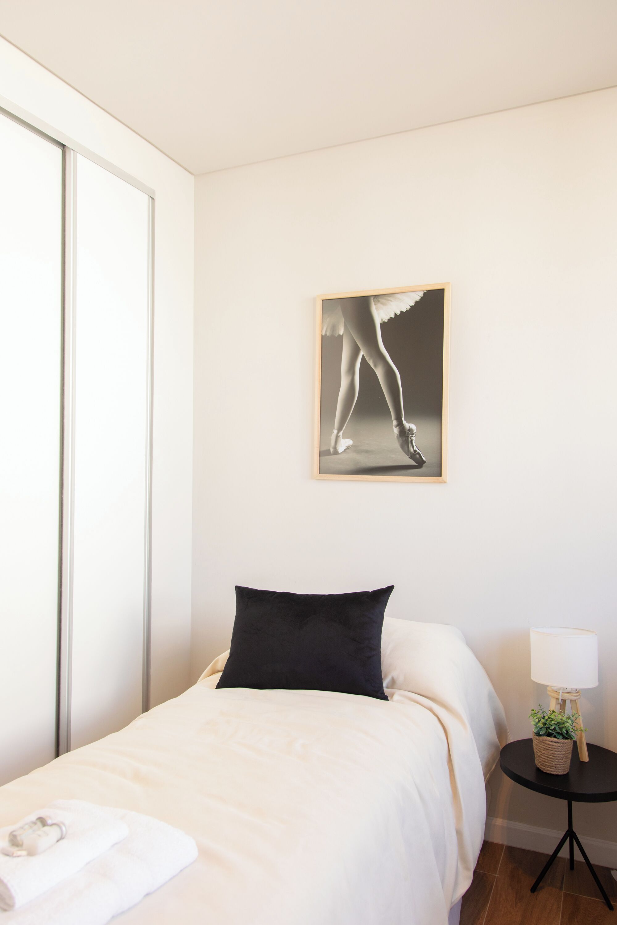 Une chambre d’hôtel avec un lit, un oreiller noir, un tableau encadr é au mur, une petite table avec une lampe et une fenêtre.