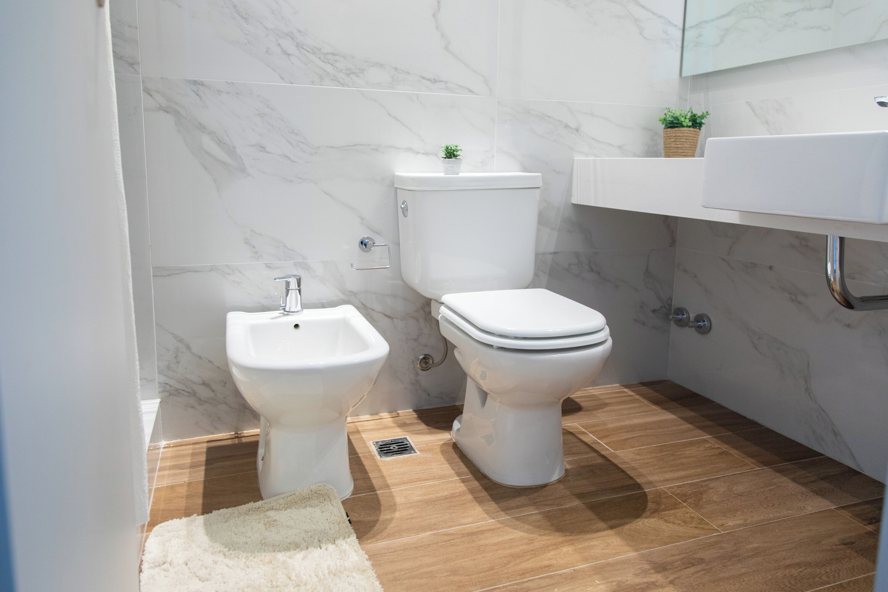 Une salle de bain moderne équipée de toilettes, d’un bidet et d’un lavabo, avec des murs en marbre et un revêtement de sol en bois.