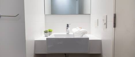 Un bagno moderno con un lavandino bianco, uno specchio sopra e una piccola pianta in vaso sul ripiano.