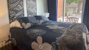 Un dormitorio con cama, ventana con cortinas, radiador y vistas al exterior.
