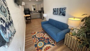 Una sala de estar con un sofá azul, un tapete estampado, una lámpara y una planta.