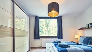 A modern bedroom with a large bed, a hanging light fixture, a window with curtains, and a radiator.