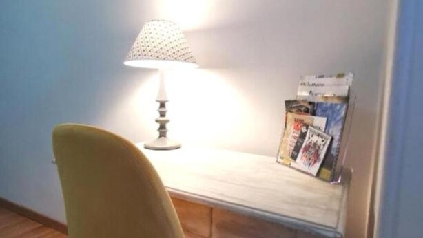 A small desk with a lamp, a chair, and a stack of magazines.