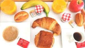 Una bandeja de desayuno con cruasanes, un plátano, una manzana, jugo y una taza de café.