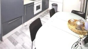Cocina compacta con gabinetes grises, microondas, estufa y lavamanos. Hay una mesa de comedor con sillas y una cesta con objetos.