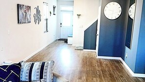 A modern living room with a sectional sofa, a staircase, and a large wall clock. - Simple Elegant Single Fam Home < DT Raleigh NCSU (Raleigh)