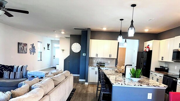 A modern kitchen with a central island, bar stools, and a dining area with a red chair. - Simple Elegant Single Fam Home < DT Raleigh NCSU (Raleigh)