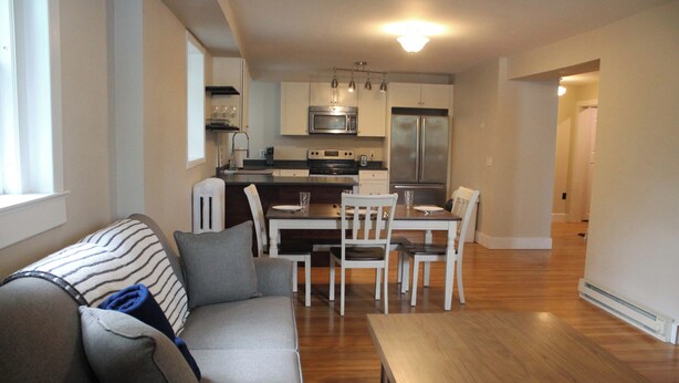 A modern kitchen with stainless steel appliances, a dining area with a wooden table and chairs, and a living room with a sofa and a coffee table.