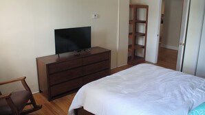 A bedroom with a bed, a dresser with a TV, a wooden chair, and a closet.