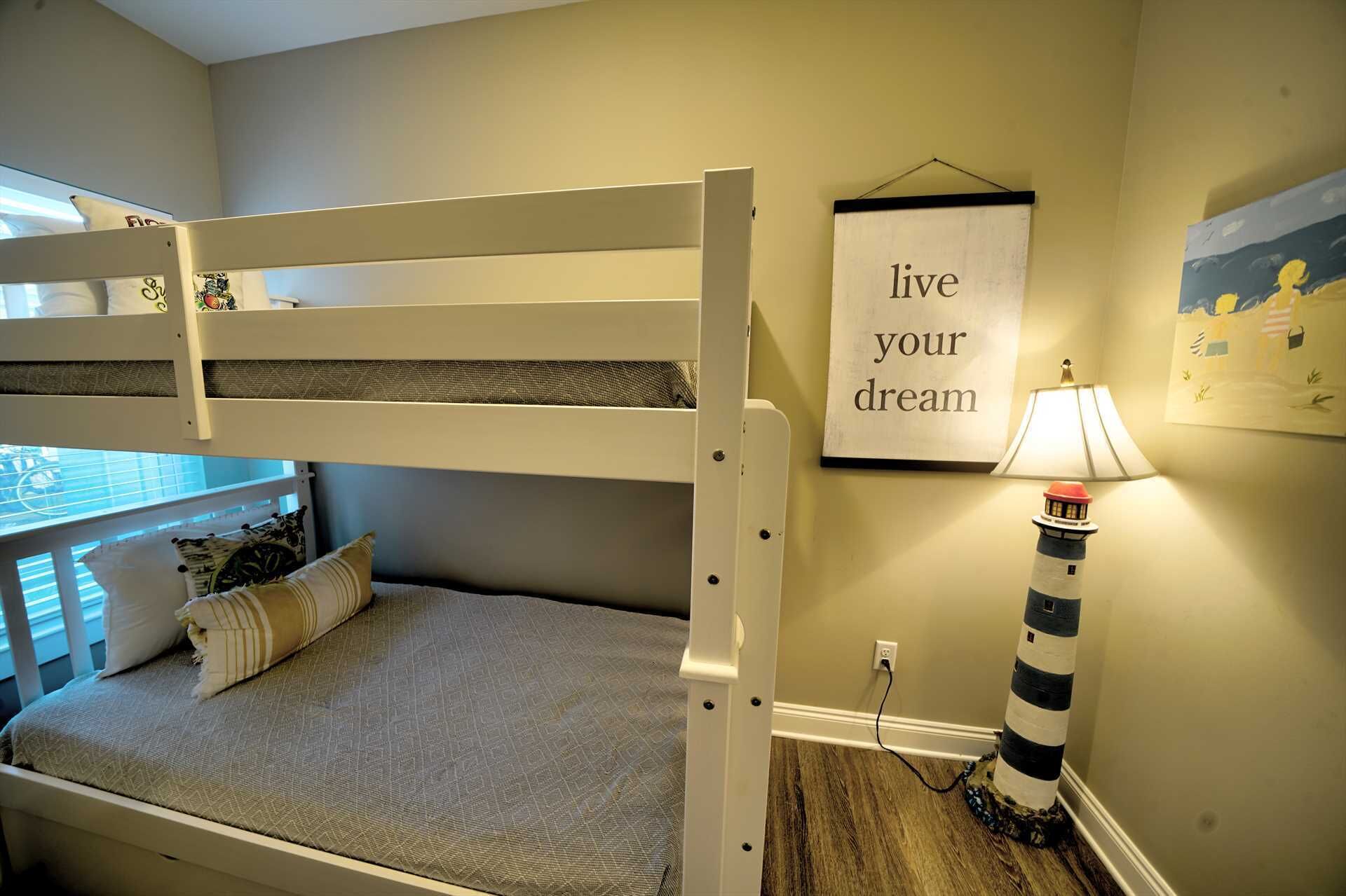 Una cama litera con colchón y almohadas, una lámpara de pared y un cartel motivacional.