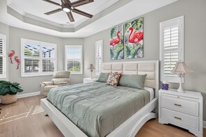 A bedroom with a bed, nightstands, a chair, a ceiling fan, and artwork on the wall. - Villa Flamingo – Tropical Waterfront Retreat with Heated Saltwater Pool (Cape Coral)