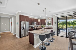 A modern kitchen with stainless steel appliances, a central island with bar stools, and a view of a swimming pool through a glass door.