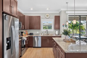 A modern kitchen with stainless steel appliances, wooden cabinets, and a large window providing a view of greenery. - Villa Flamingo – Tropical Waterfront Retreat with Heated Saltwater Pool (Cape Coral)
