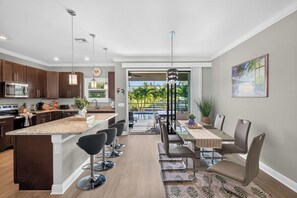 Una cocina moderna con una isla central, taburetes de bar y un comedor con vista a una piscina.