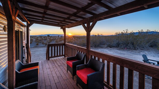 Una terraza techada con sillas de mimbre y vista al atardecer sobre un paisaje desértico.