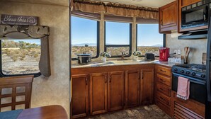 Una cocina con armarios de madera, estufa, microondas y ventana con vista al desierto.