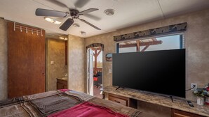Un dormitorio con una cama, ventilador de techo, televisor y puerta de madera.