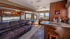 Un interior de autocaravana acogedor, con un sofá de cuero, una mesa de comedor y una zona de cocina con barra.