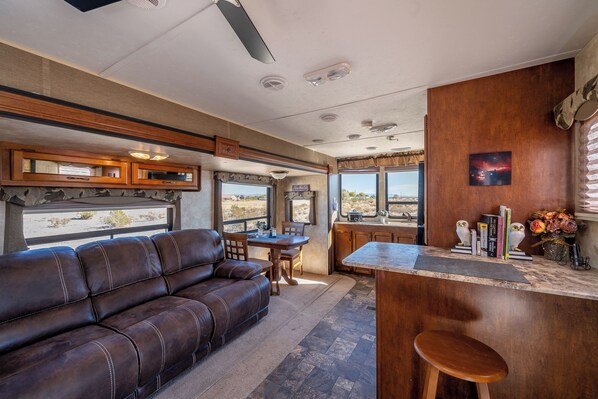 Un interior de autocaravana acogedor, con un sofá de cuero, una mesa de comedor y una zona de cocina con barra.
