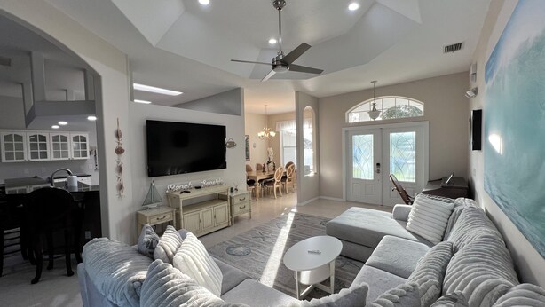 A spacious living room with a large flat-screen TV, a ceiling fan, and a comfortable seating area with a sofa and a coffee table.
