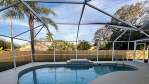 A covered swimming pool with a wooden fence and palm trees in the background.