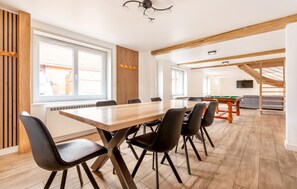 Um quarto amplo com uma longa mesa de madeira, cadeiras pretas, mesa de bilhar e uma escada com vigas de madeira.