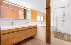 Uma casa de banho moderna com toucador de madeira, um espelho grande e cabine de duche em vidro.