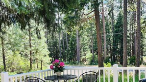 Un patio con una mesa y sillas, una cerca blanca y vistas a árboles altos.