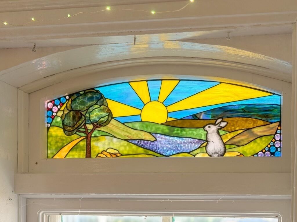 Un vitrail représentant un soleil, un arbre et un lapin.