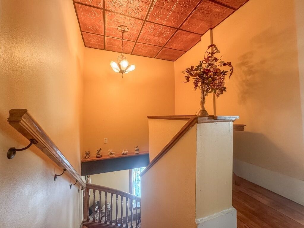 A staircase with a wooden handrail, a light fixture, and a vase with flowers on the landing.
