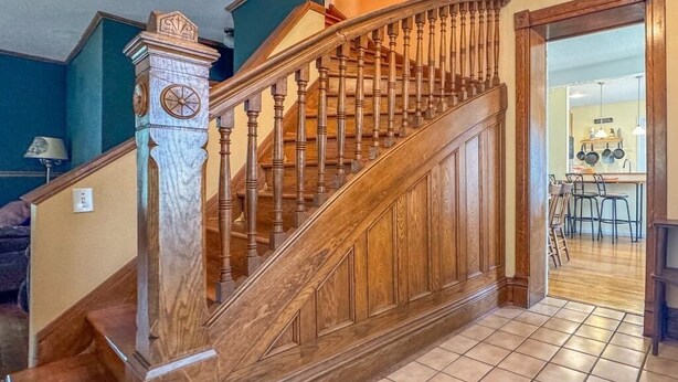 Una escalera de madera con un reloj, que conduce a una zona de cocina con un cartel que dice 'Aquí se miman a los nietos'.