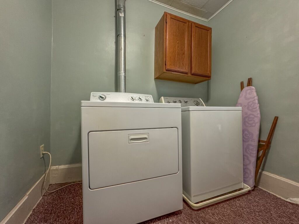 A laundry room with two stacked washers and dryers, a wooden cabinet above, and a purple towel hanging on a chair.