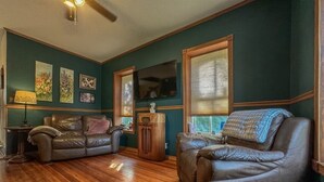 A living room with two leather sofas, a wooden floor, a television, and artwork on the walls.