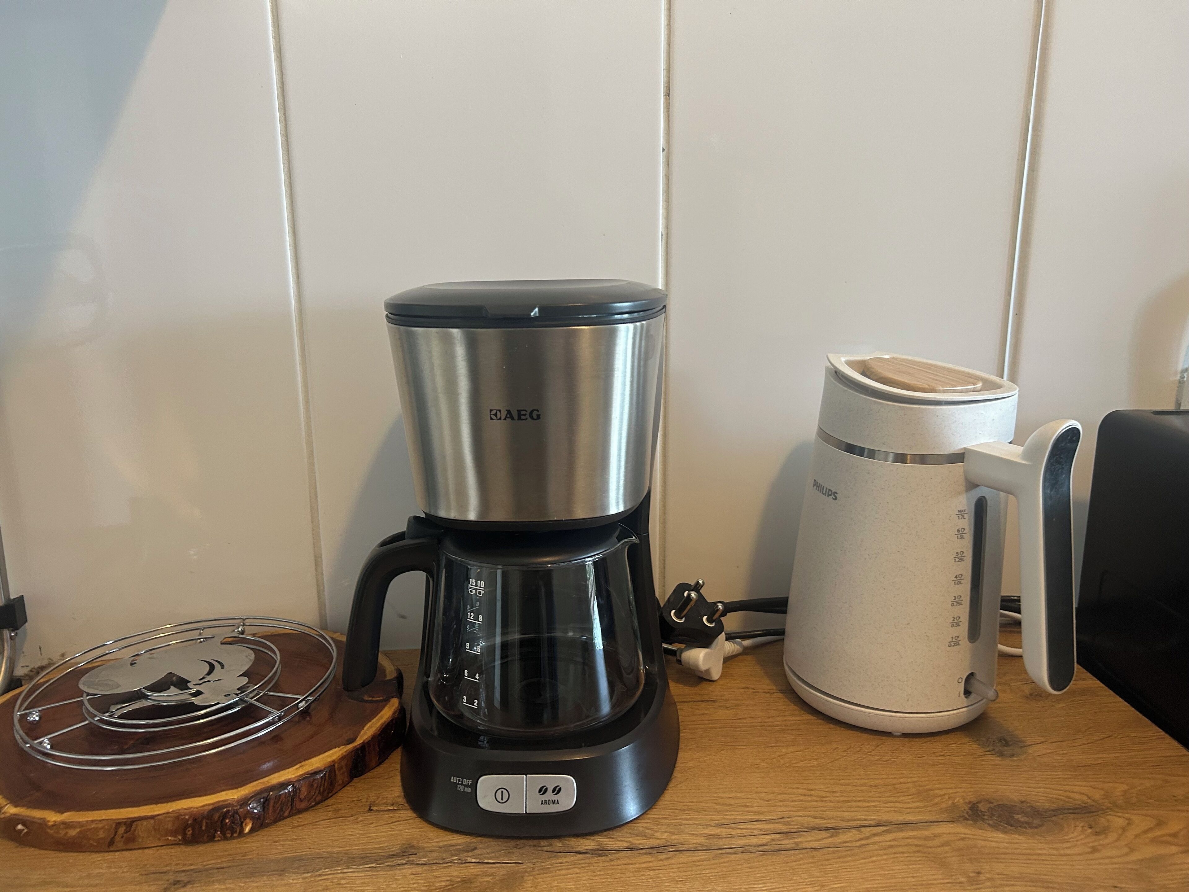 Una cafetera, una taza blanca y una bandeja de madera sobre una mesa de madera.