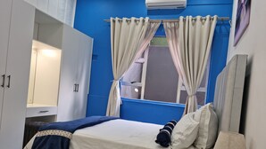 Ein Schlafzimmer mit Bett, Nachttisch, Lampe, Kleiderschrank und einem Fenster mit Vorhängen.