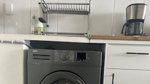 Eine kleine, moderne Küche mit integriertem Waschmaschine, einer Kaffeemaschine und einem Wäscheständer.
