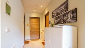 A hallway with a wooden door, a white cabinet, and a refrigerator. There are framed pictures on the wall and a small plant on the cabinet. - Teo's House - Navigli Apartments (Milano)
