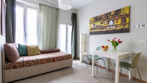 A living room with a sofa, a dining table with chairs, a painting on the wall, and a vase with flowers. - Teo's House - Navigli Apartments (Milano)