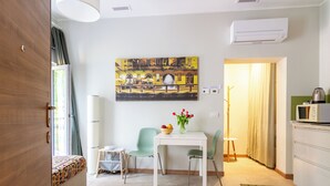 A modern hotel room with a bed, a dining area with a table and chairs, a painting on the wall, and a kitchenette. - Teo's House - Navigli Apartments (Milano)