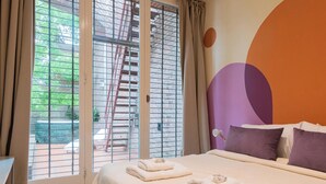 Une chambre d’hôtel avec un lit, des oreillers et une vue par une fenêtre ornée d’une grille métallique.