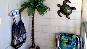Une salle de bain avec un sol carrelé de carreaux blancs, un palmier en pot, un climatiseur fixé au mur et un chariot à bagages.