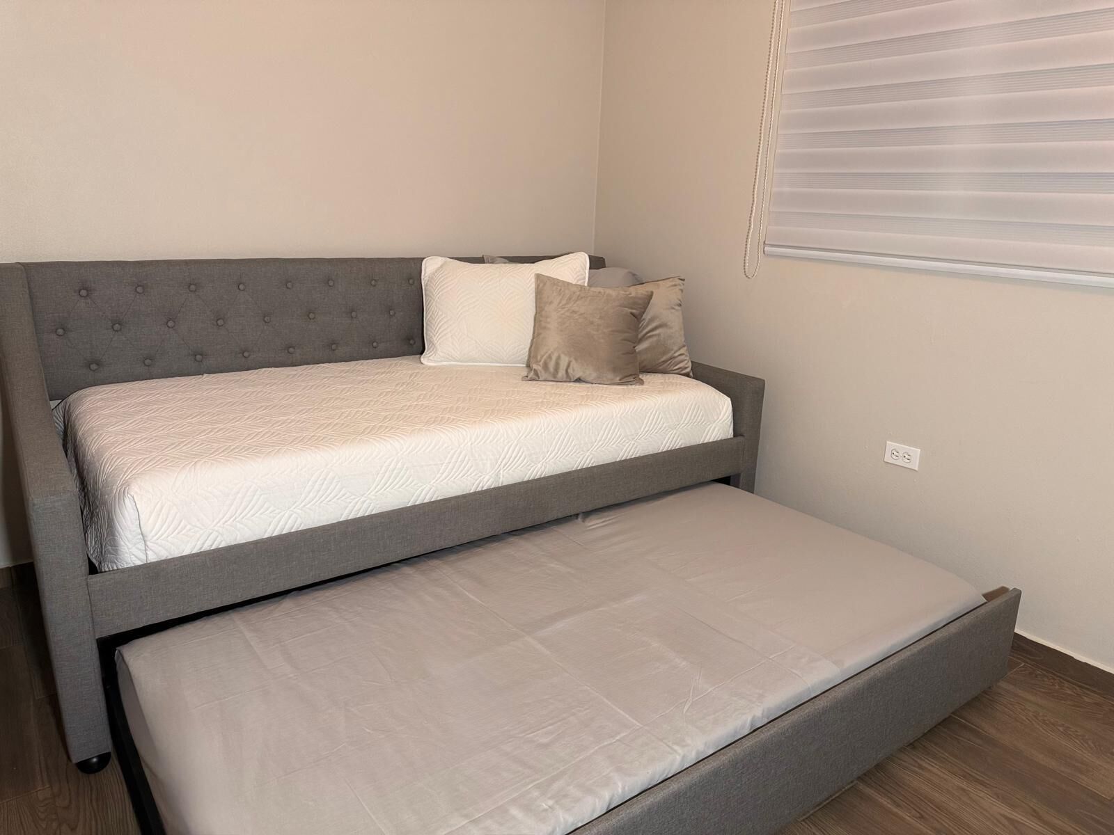 A single bed with a grey headboard and a lower platform bed.